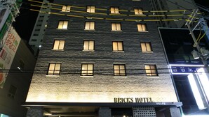 Um hotel com vários andares, janelas iluminadas e uma placa com o nome 'Bricks Hotel'.