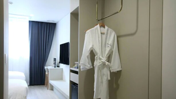 Quarto de hotel com cama, escrivaninha, cadeira, televisão e roupão pendurado na parede.
