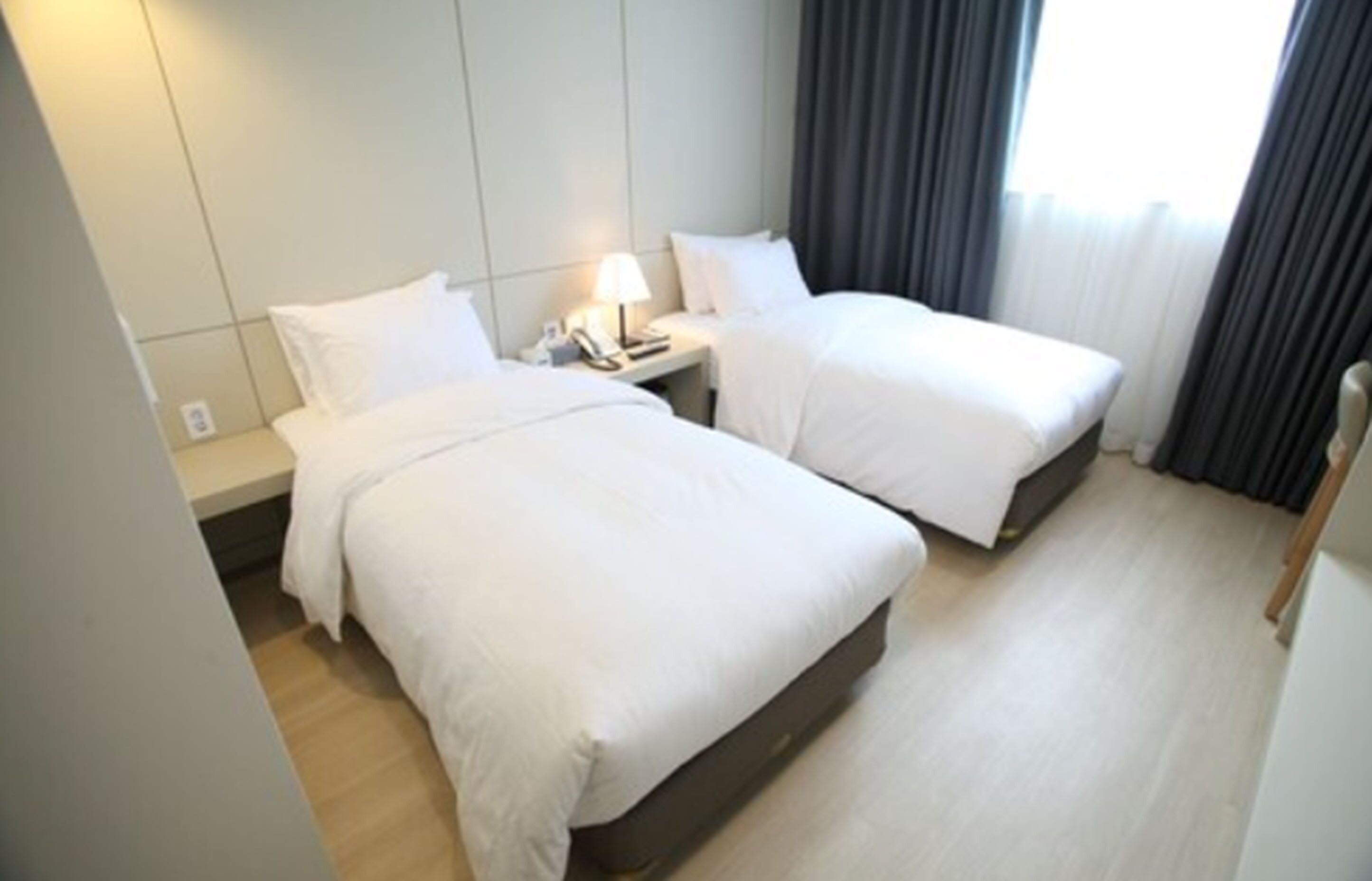 Una habitación de hotel con dos camas, una mesita de noche con lámpara y una ventana con cortinas.