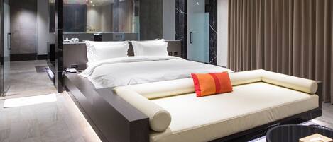 Quarto de hotel moderno com uma cama grande, mesa de cabeceira, espelho e vista para a cidade.