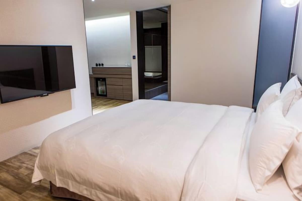 A modern bedroom with a large bed, a flat-screen TV mounted on the wall, and a walk-in closet with a mirror.