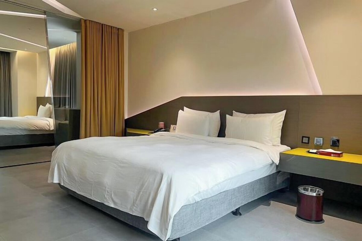 Una habitación de hotel moderna con una cama grande, mesitas de noche y un espejo.