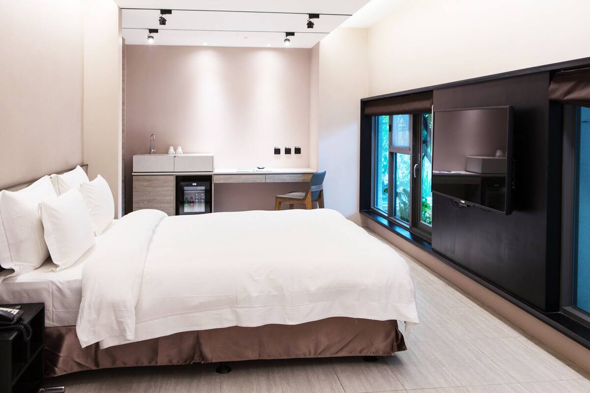A modern hotel room with a large bed, a desk with a sink, and a TV mounted on the wall.