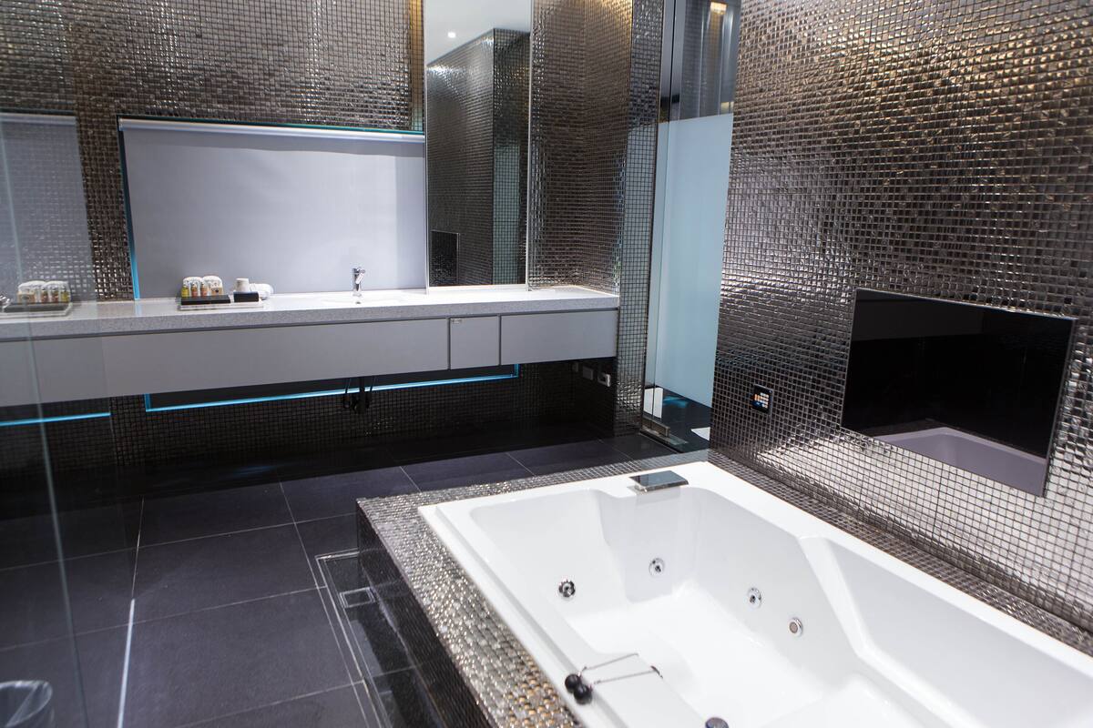A modern bathroom with a large bathtub, a glass-enclosed vanity, and a tiled wall.
