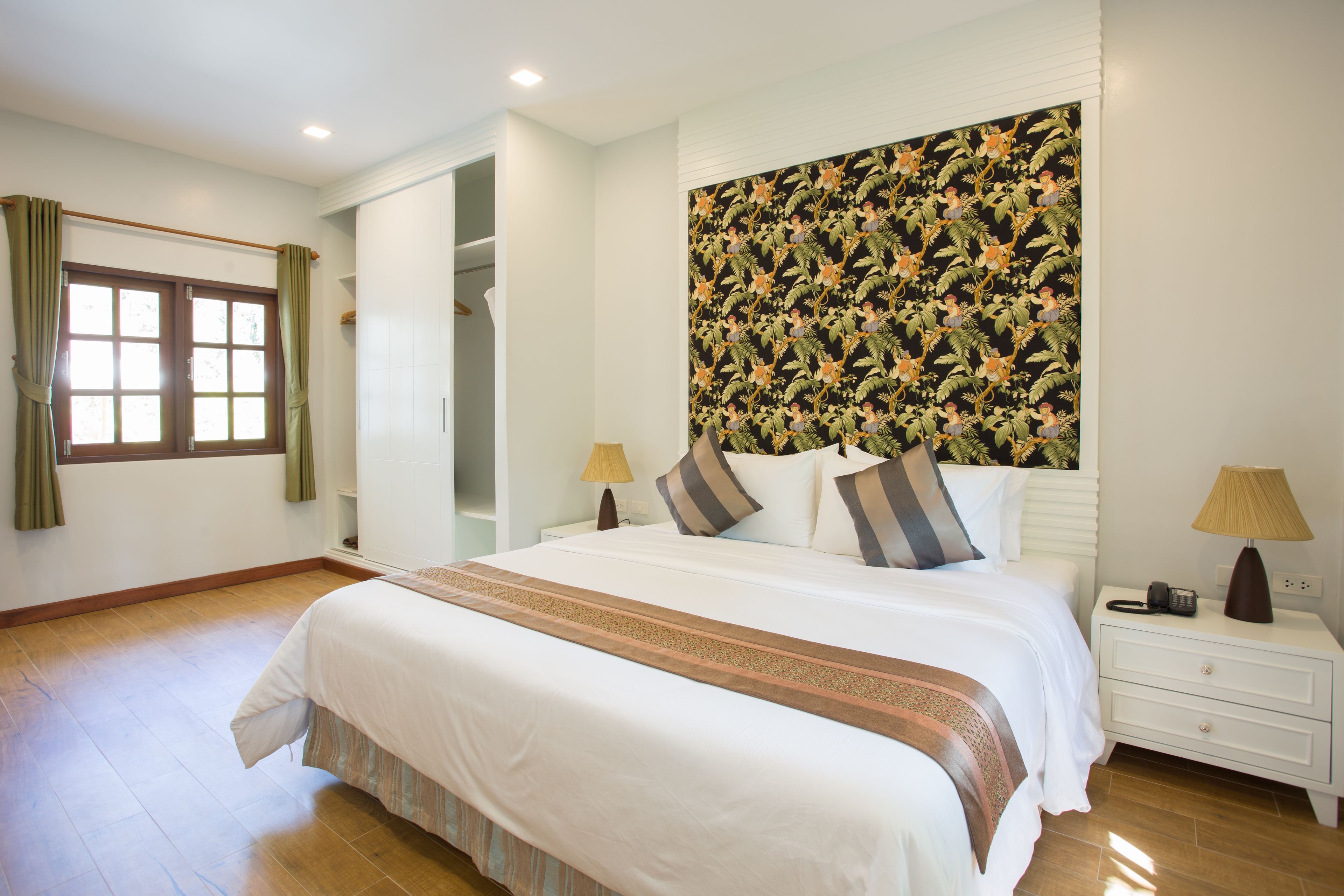 A neatly arranged bedroom with a large bed, a nightstand, a lamp, and a window with curtains.