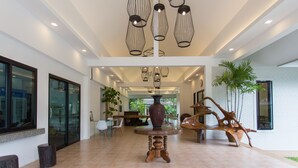 Un hall d’entrée spacieux avec un plafond haut, des luminaires modernes, une grande table en bois au centre et un grand vase.