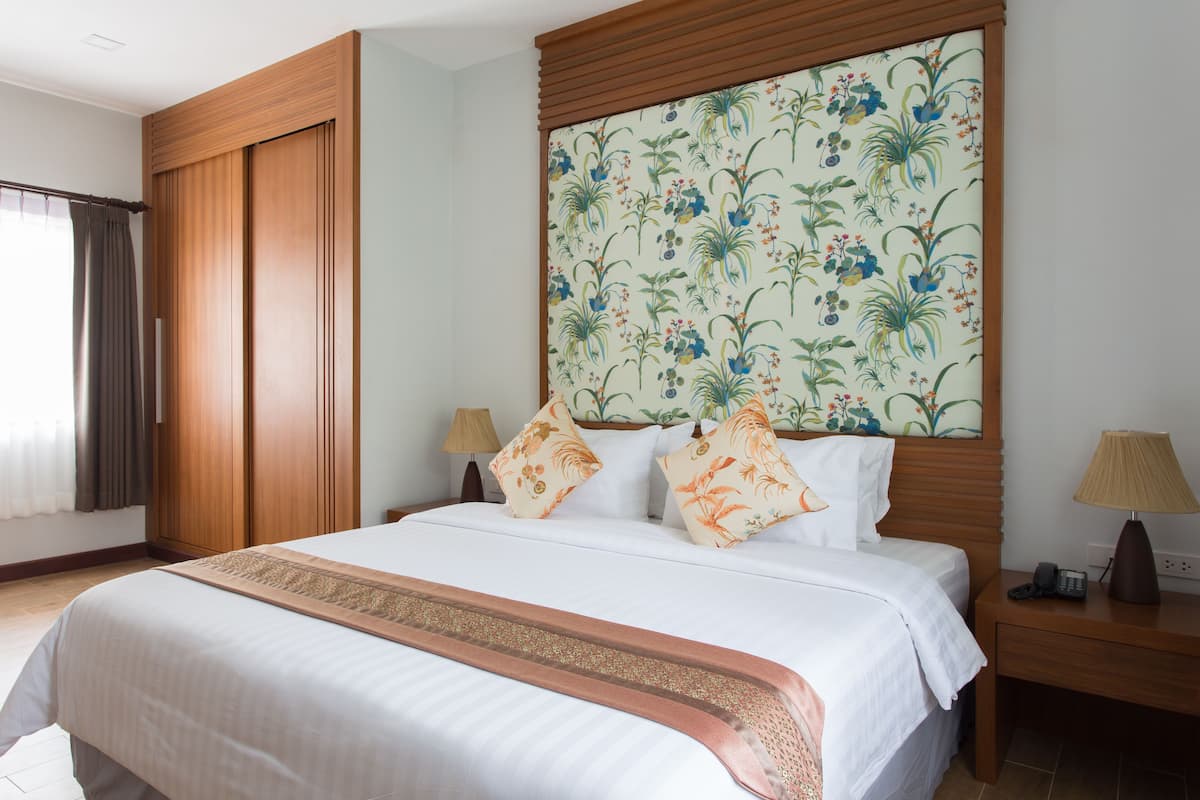 A hotel room with a large bed, wooden wardrobe, and a floral-patterned headboard.