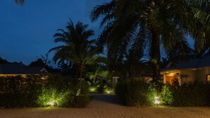 Un chemin menant à un bâtiment entouré de palmiers et éclairé par des lampes de jardin.
