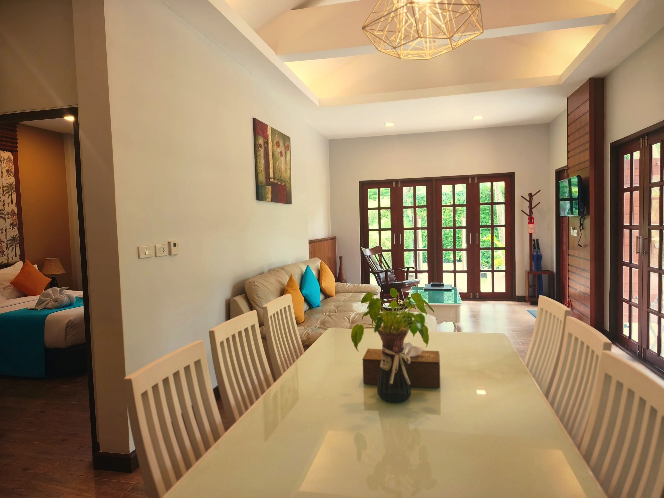 A spacious room with a dining table, chairs, a sofa with cushions, a painting on the wall, and a large window with a view.