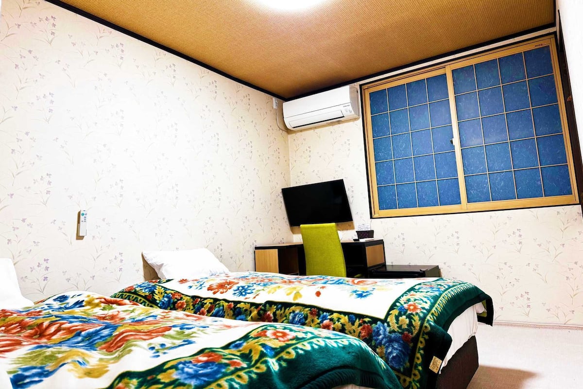 A bedroom with a bed, a desk, a chair, and a window with blue-tinted glass.