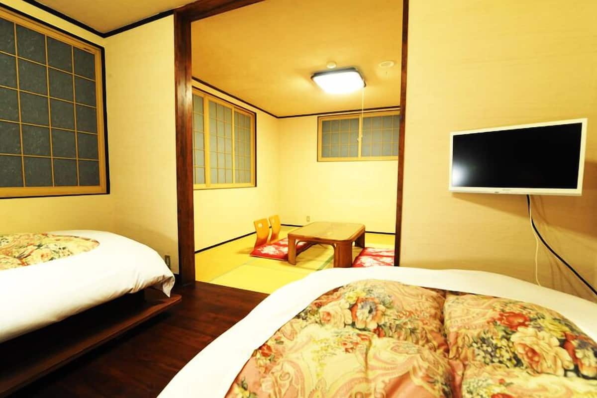 Ein traditioneller japanischer Raum mit Tatami-Bodenbelag, Futon-Bett, Fernseher und einer Schiebetür.