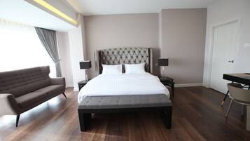 A modern hotel room with a large bed, a sofa, a desk, and a chair.