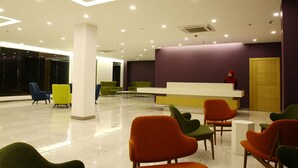 Un área de recepción moderna con un mostrador, varias sillas coloridas y un amplio ventanal al fondo.