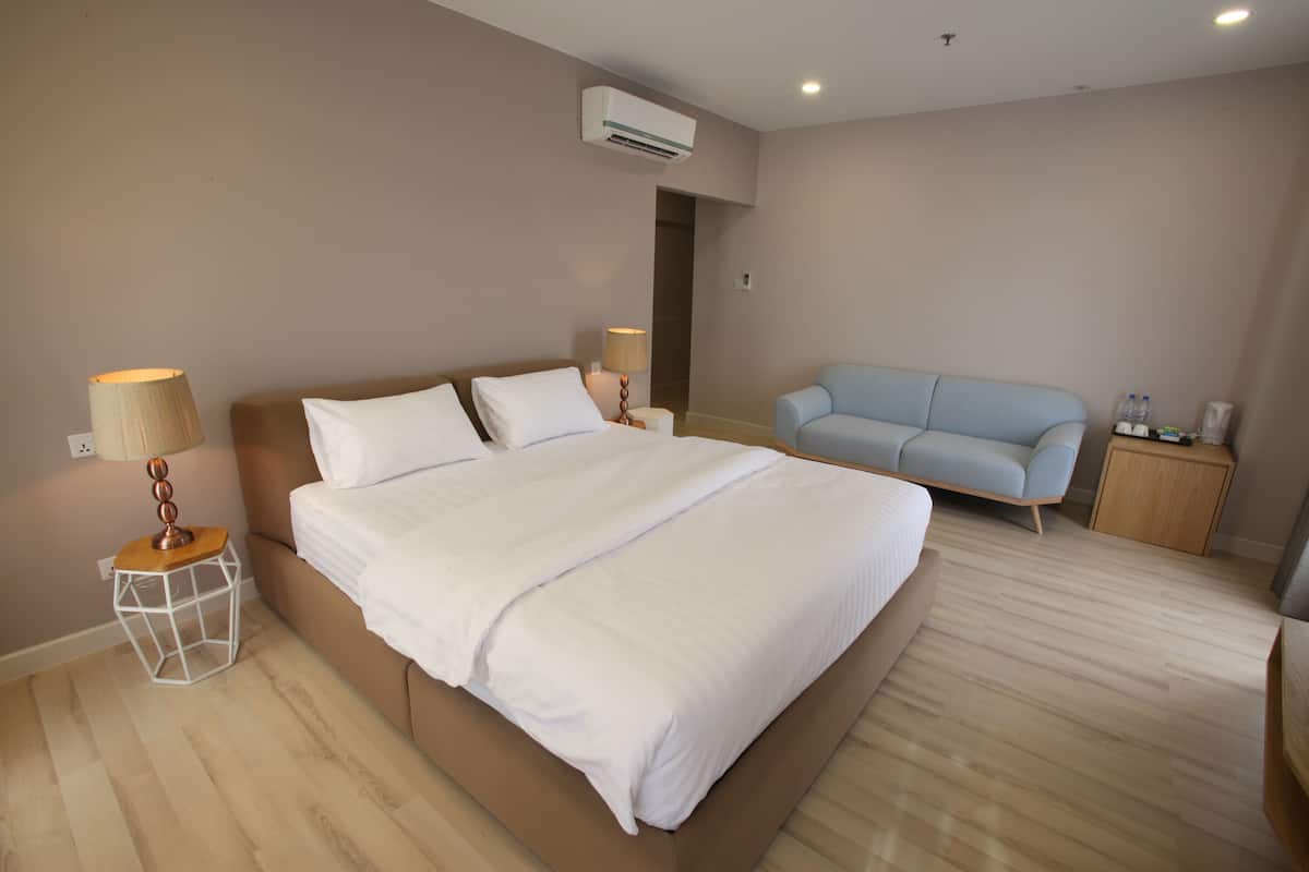Quarto com uma cama grande, uma mesinha de cabeceira com abajur, uma poltrona azul e um armário de madeira.