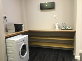 Un área de lavandería con lavadora, microondas y dispensador de agua en un estante.
