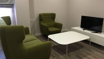 Una sala de estar moderna con sillones tapizados en verde, una mesa de centro blanca y un televisor de pantalla plana sobre un mueble blanco.