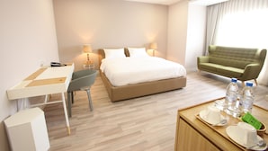 Habitación de hotel con cama, escritorio, silla y una mesita con botellas de agua y un paquete verde.