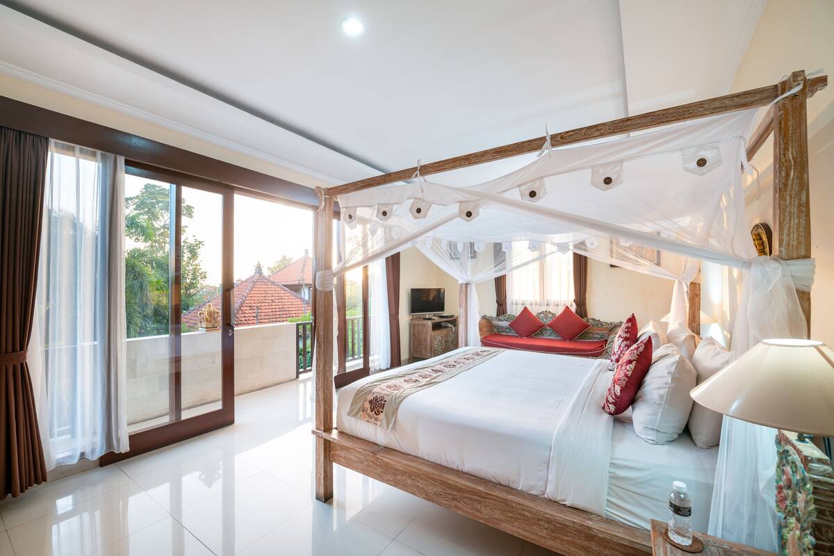 Un dormitorio amplio con cama con dosel, televisión y balcón con vista a la ciudad.