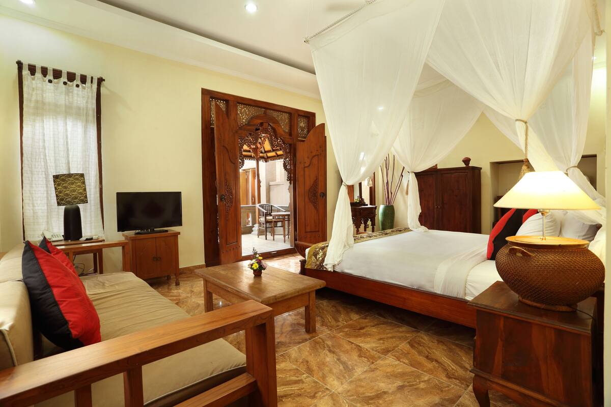 Un dormitorio con una cama, televisor, escritorio, silla y mesita de noche de madera.