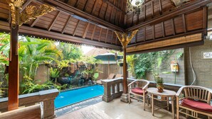 Un espacio al aire libre cubierto con piscina, muebles de madera y plantas tropicales.