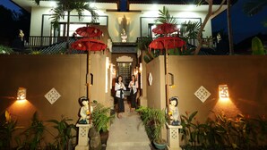 A well-lit entrance with a pathway leading to a house, surrounded by potted plants and decorative statues. - Ashanti Villa Ubud (Ubud)