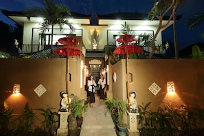 A well-lit entrance with a pathway leading to a house, surrounded by potted plants and decorative statues. - Ashanti Villa Ubud (Ubud)