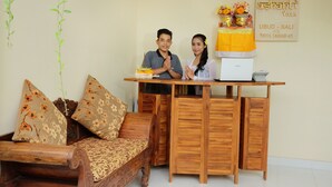 A wooden sofa with floral cushions, a small table with a laptop, and a wall-mounted sign with text. - Ashanti Villa Ubud (Ubud)