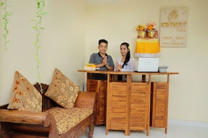 A wooden sofa with floral cushions, a small table with a laptop, and a wall-mounted sign with text. - Ashanti Villa Ubud (Ubud)