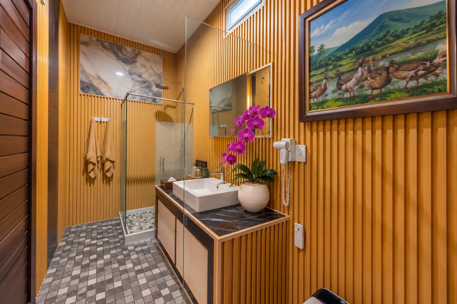A bathroom with a glass shower enclosure, a marble sink, and a potted orchid.