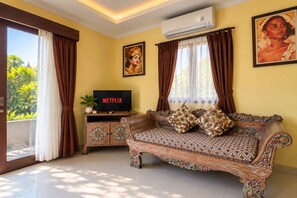 A living room with a sofa, a television displaying 'NETFLIX,' and a wall-mounted air conditioner. - Ashanti Villa Ubud (Ubud)