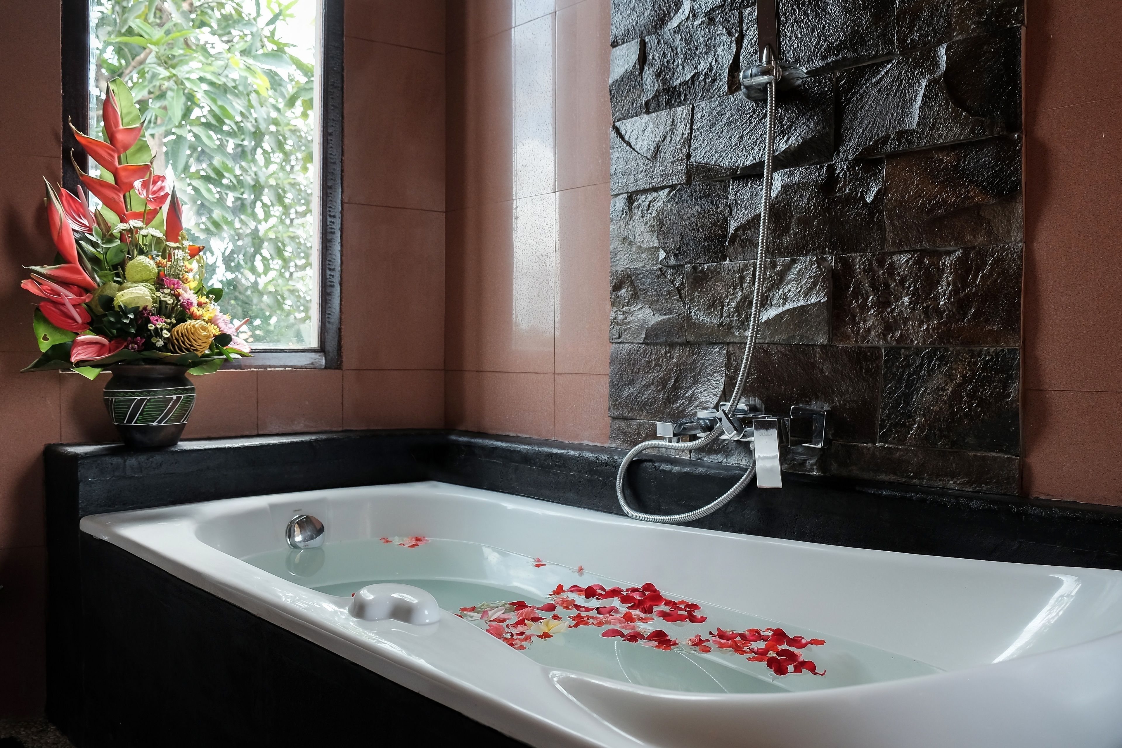 A bathroom with a bathtub, a shower, and a window with a flower arrangement.
