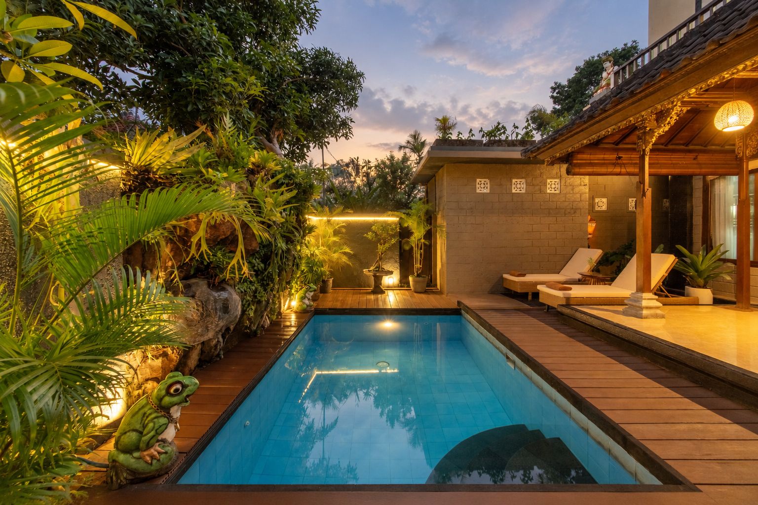 A swimming pool with a wooden deck, surrounded by lush greenery and a stone wall.