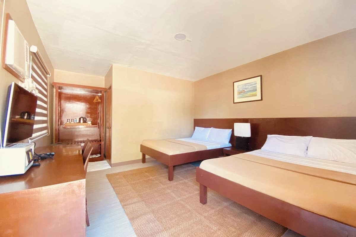 A hotel room with two beds, a desk, a chair, a television, and a bathroom visible through an open door.