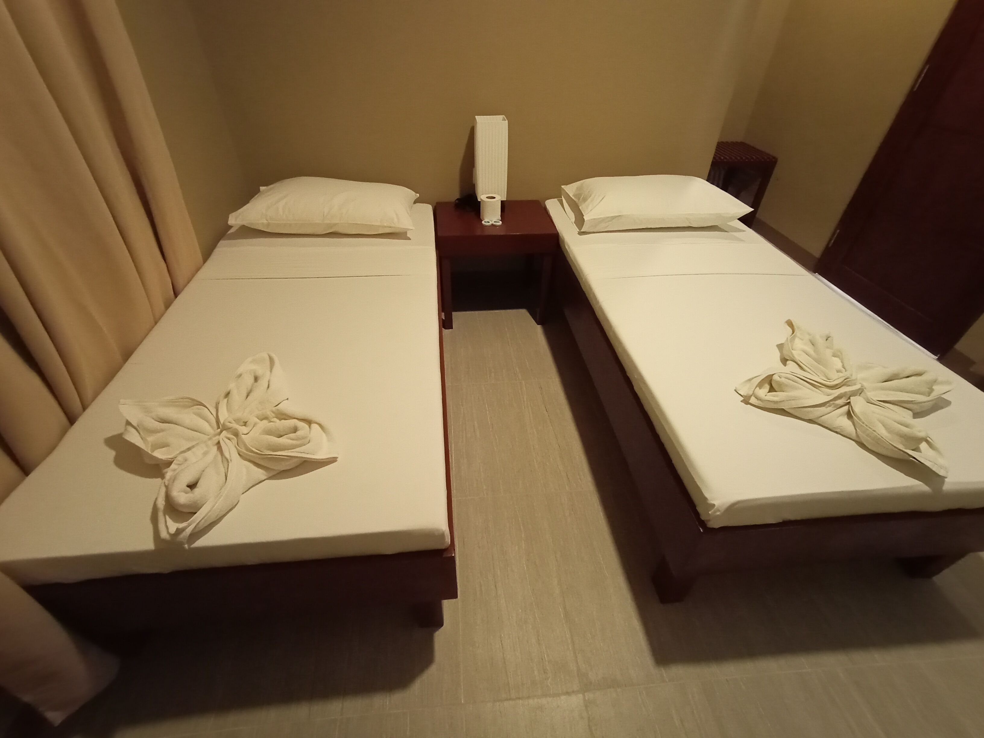 A hotel room with two single beds, each with a neatly folded towel and pillow.