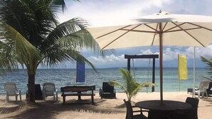A beachside seating area with a table and chairs, a large umbrella, and a palm tree. - Anaya Beach Resort (Bantayan)