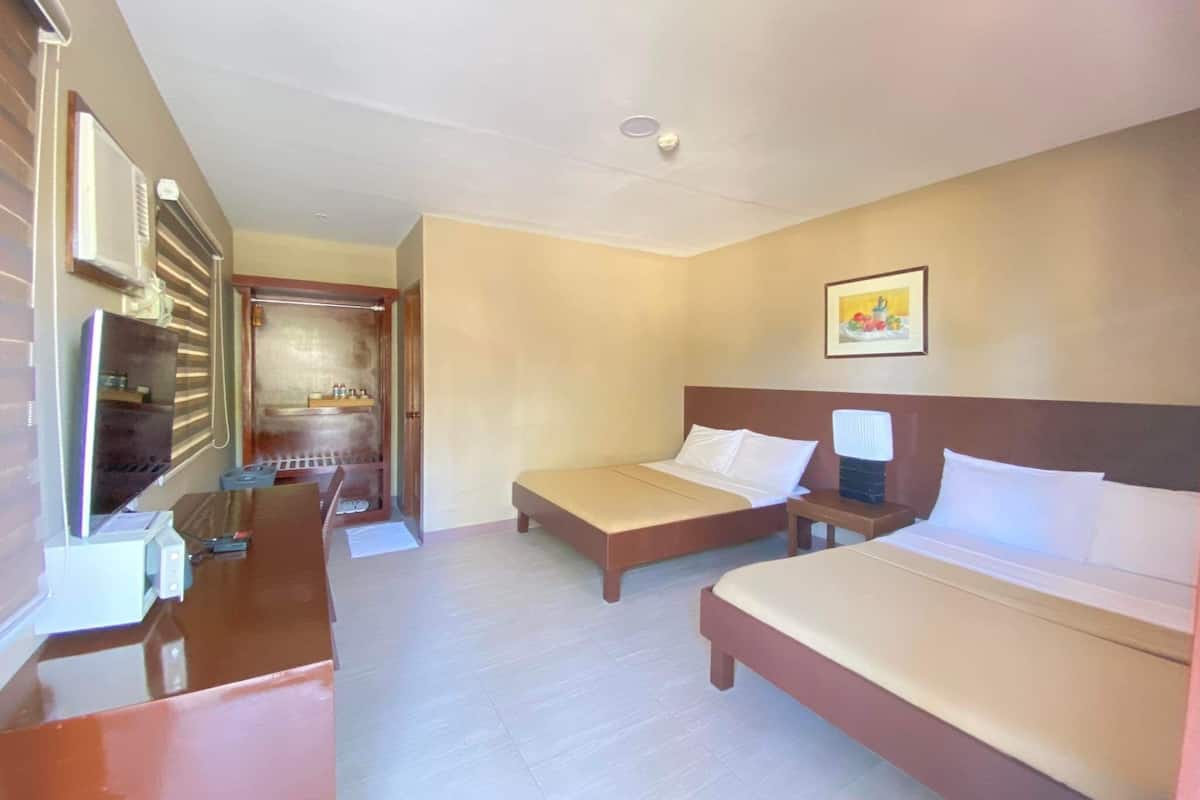 A hotel room with two beds, a desk, a chair, a TV, and a bathroom visible through an open door.