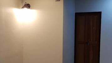 Una habitación con puerta de madera, un accesorio de iluminación en el techo y una lámpara pequeña empotrada en la pared.