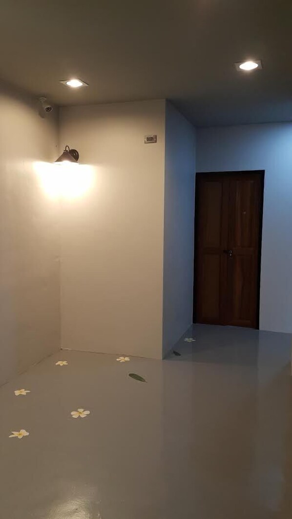 A room with a wooden door, a light fixture on the ceiling, and a small wall-mounted light. - Chomtrang (Trang)