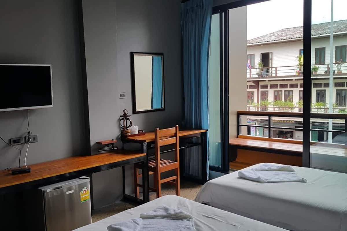 A hotel room with a bed, a desk, a chair, a TV, and a window with a view of buildings.