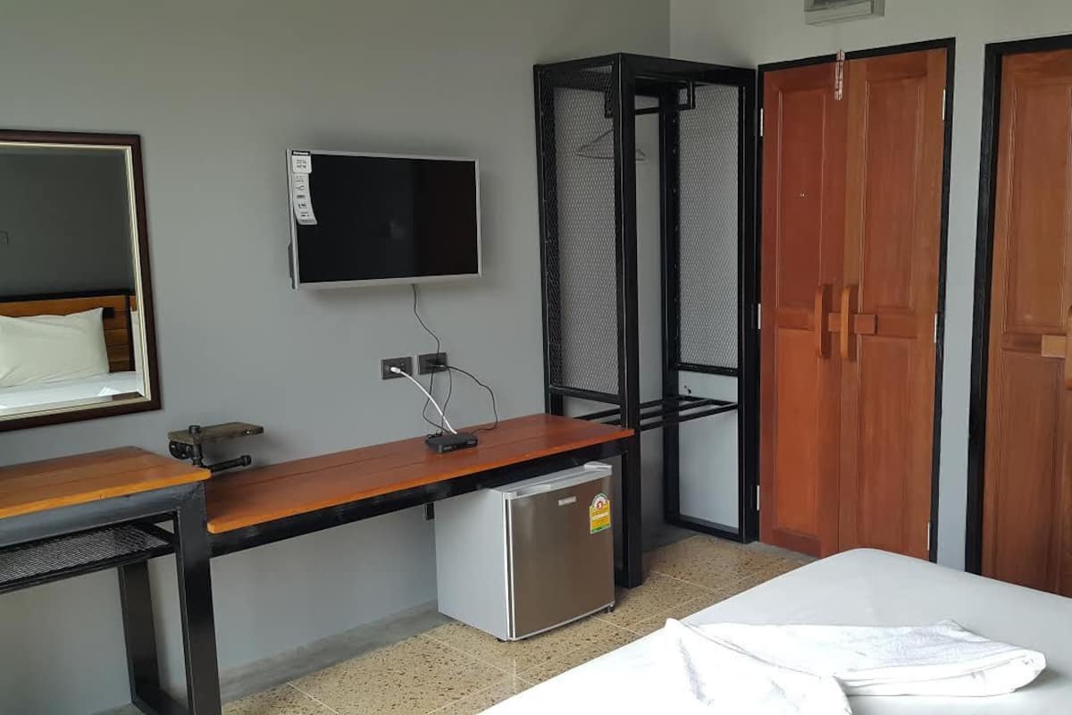 A hotel room with a bed, a desk with a computer, a small refrigerator, a TV mounted on the wall, and two wooden wardrobes.