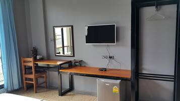 Una habitación con escritorio de madera, una silla, televisor montado en la pared y un refrigerador pequeño.