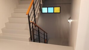 Un escalier avec une rampe en bois et des balustres noires, menant à un palier où se trouvent un interrupteur et un luminaire fixé au mur.