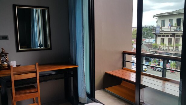 Une pièce comprenant un bureau, une chaise, une fenêtre donnant sur un immeuble et un rideau.