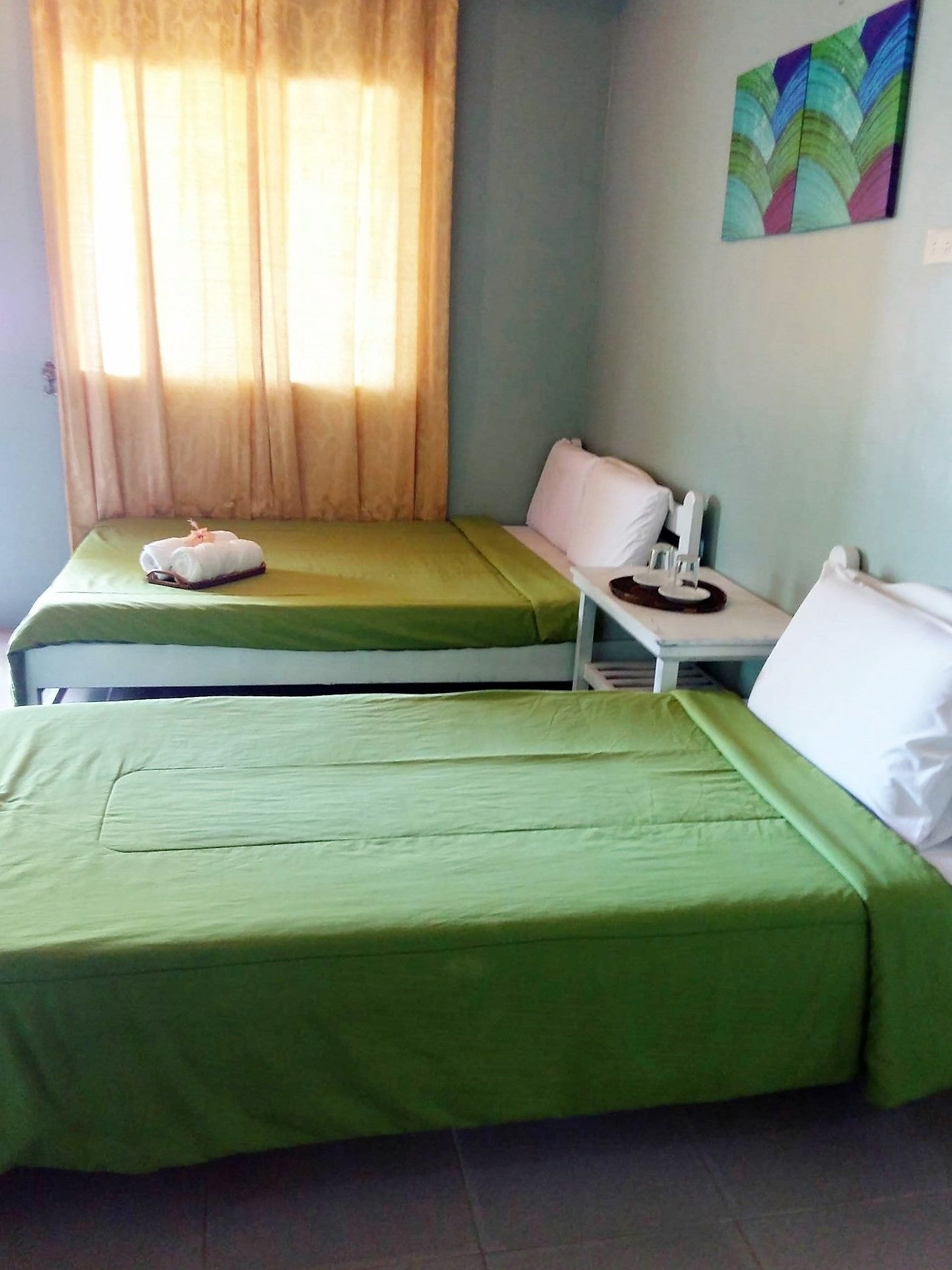 Una habitación con dos camas, una mesita, una silla y un ventanal con cortinas.