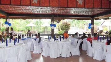 A covered outdoor dining area with white tablecloths and blue and white balloons.