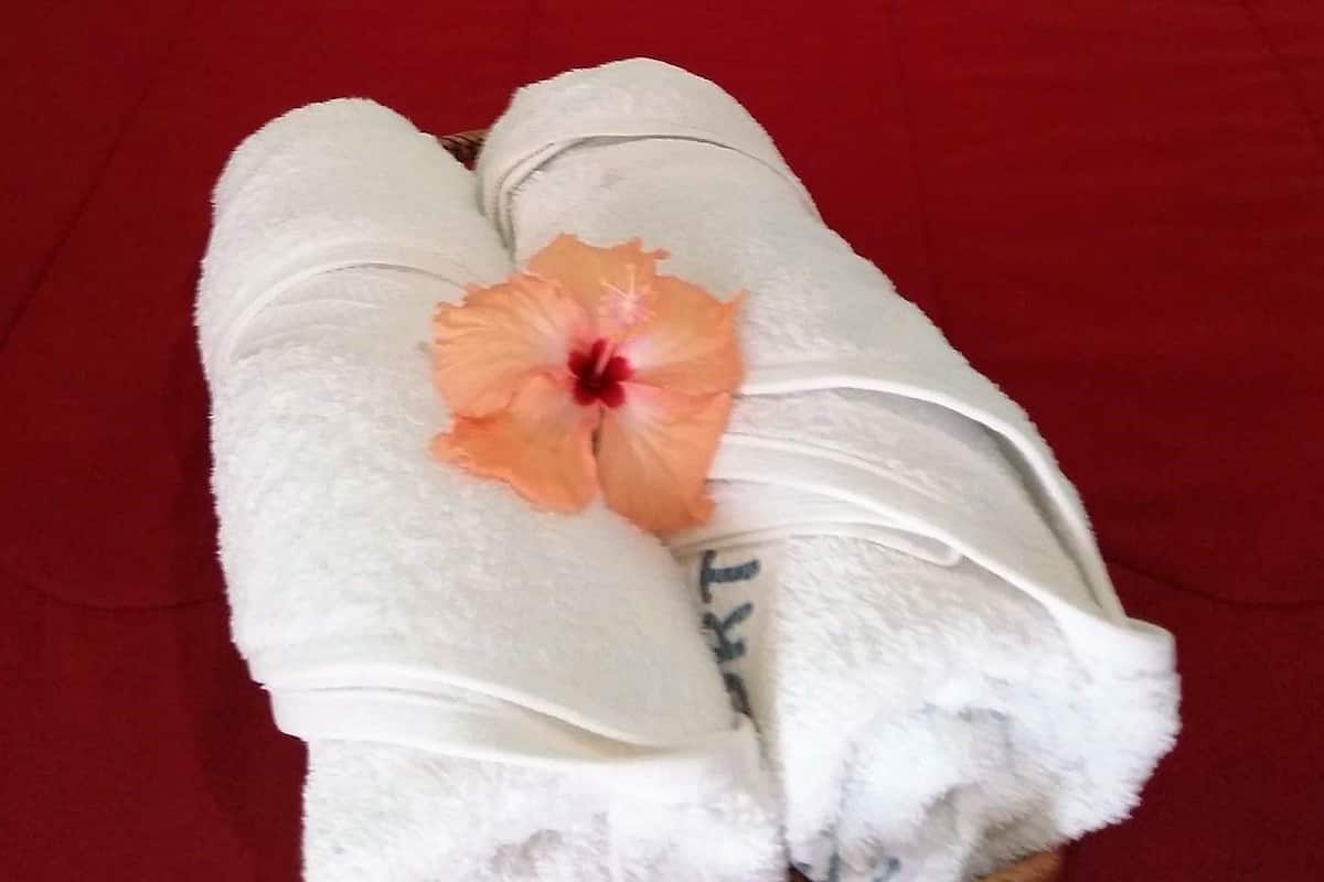 Un lit avec une couvre-lit rouge, des oreillers blancs et une serviette ornée d’une fleur d’hibiscus.