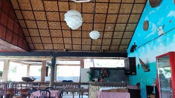 Um restaurante com telhado de palha, mesas de madeira e uma parede azul com um mural.