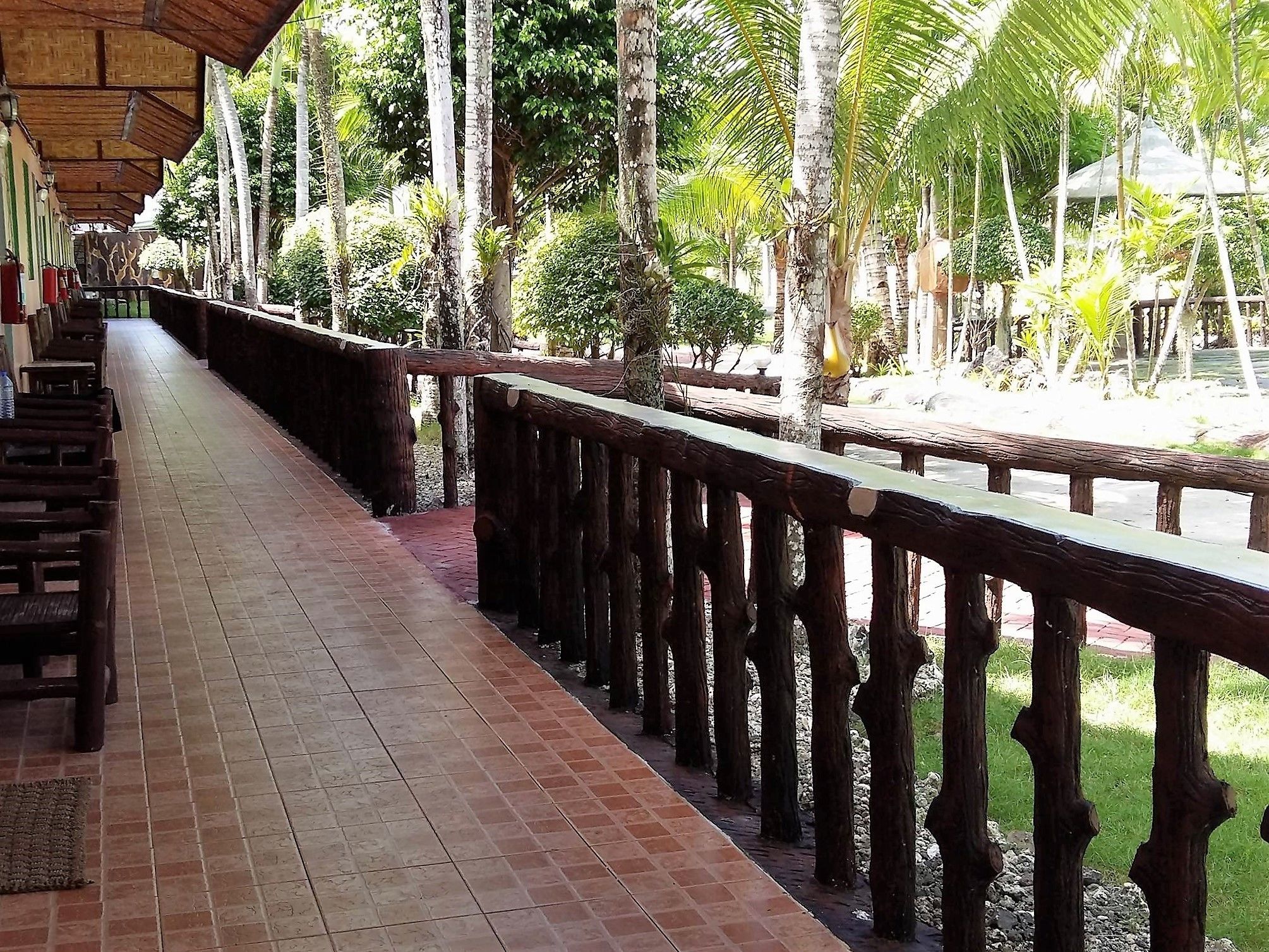 A covered walkway with wooden railings, lined with benches and surrounded by lush greenery.