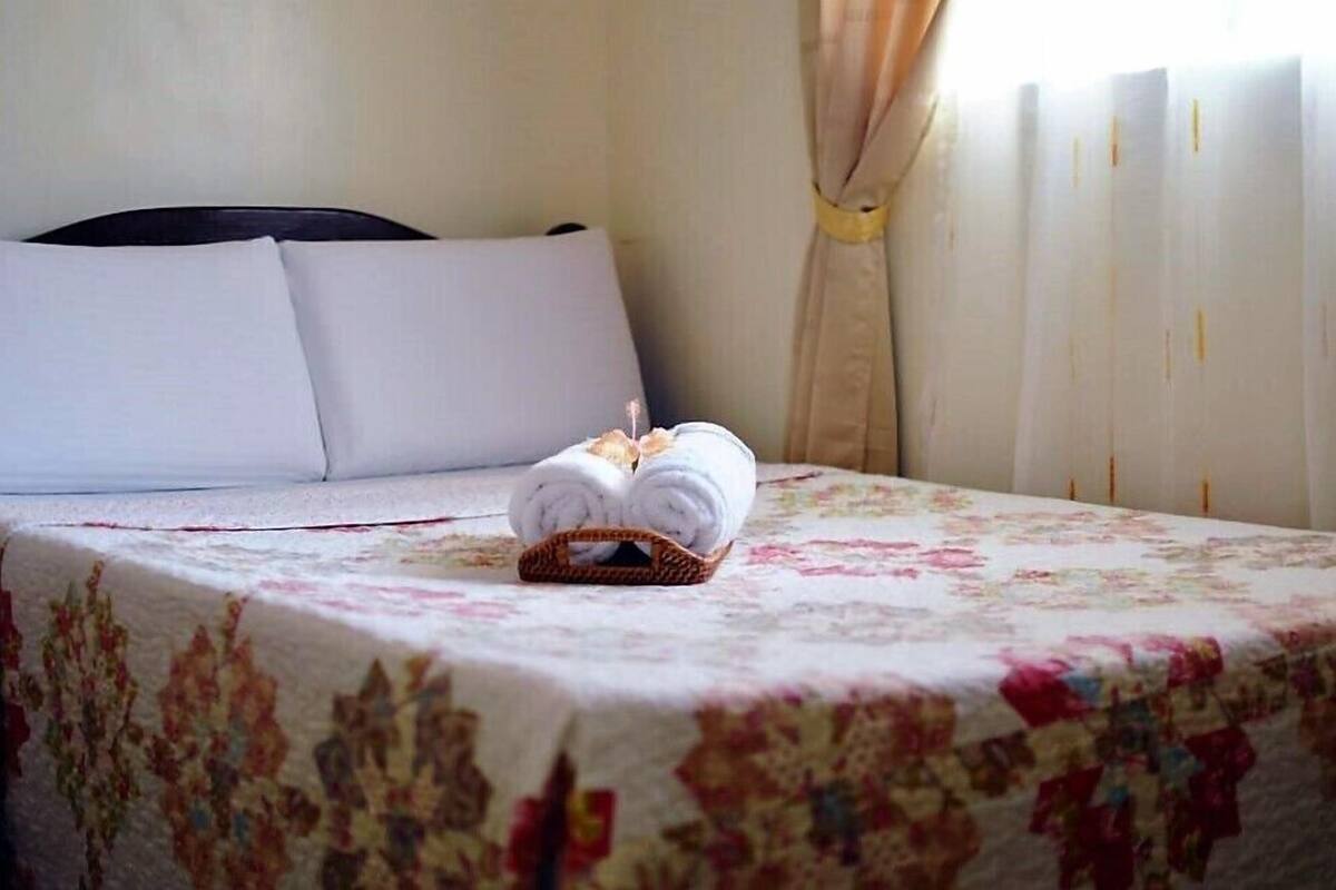 Un lit bien fait, avec des draps blancs, une couvre-lit à motifs floraux et un panier rempli de serviettes pliées posé sur le lit.