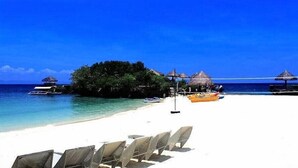 Una playa con arena blanca, agua azul cristalina y construcciones de techo de paja.
